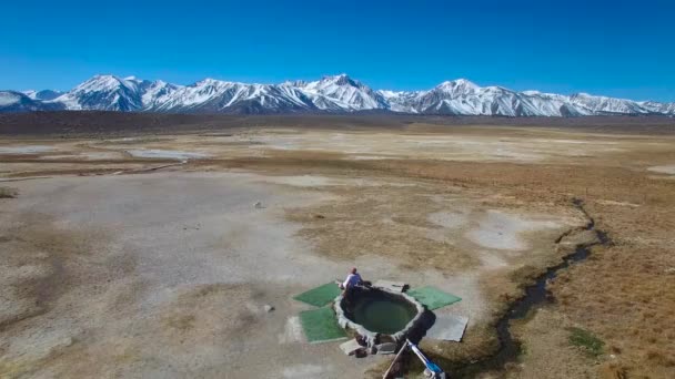 カリフォルニア州マンモス近くのシエラネバダ山脈の自然温水プールの男の上の航空機 — ストック動画