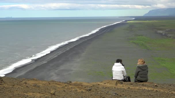两名妇女坐在悬崖上俯瞰冰岛的Dyrholahey黑色沙滩 — 图库视频影像