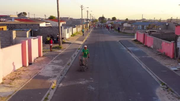 通りを歩く男とショッピングカートと南アフリカの町の通りのシーンの上に空中 — ストック動画