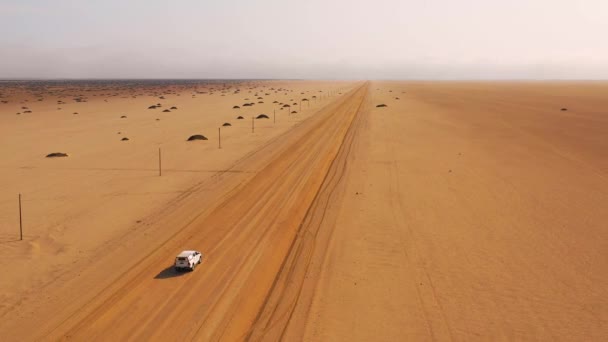 遠くに霧や霧のある平らな砂漠を横切る未舗装の道路上のサファリ車両の素敵な高い航空機 ナミビア — ストック動画