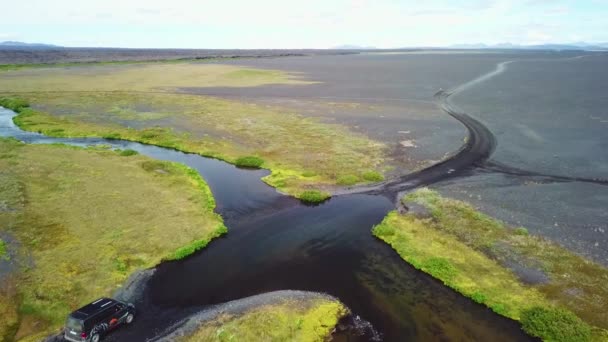 アイスランドの高地の川を流れる黒いバンの上の空中 — ストック動画