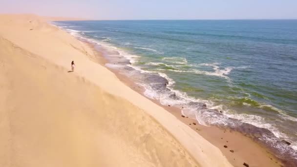 ナミビアのスケルトン海岸の壮大な砂丘を歩く女性を解放したモデルの上に空中 — ストック動画