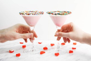 Erkek ve kadın elleri pembe alarak süt kokteyl, yakın çekim. Reçelli kalpler ile dekore edilmiştir. Saint Sevgililer günü.