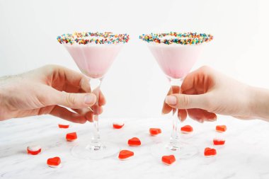 Erkek ve kadın elleri pembe alarak süt kokteyl, yakın çekim. Reçelli kalpler ile dekore edilmiştir. Saint Sevgililer günü.