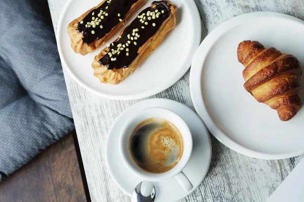 White plate with Coffee eclairs and croissant with cup of fresh black coffee — Stock Photo, Image