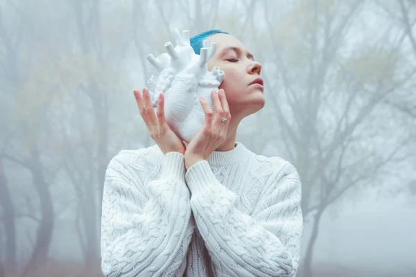 Güzel bir kız, sisli bir arka planda, kısa mavi saç stiliyle kalbini dinliyor..