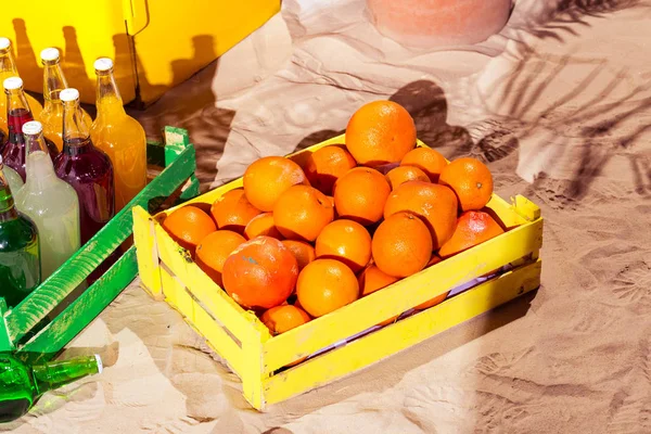 Caja de madera naranja y botellas de limonada en verano tiempo soleado en la playa del océano con hojas de palma Imagen de archivo