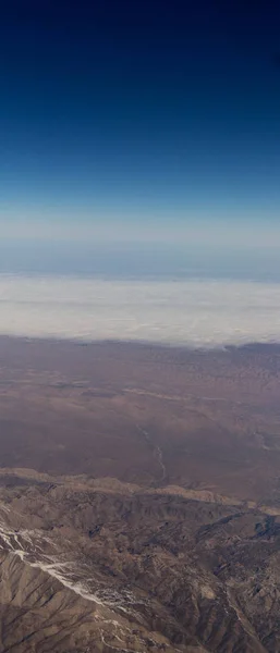 Nuvens montanhas e céu como visto através da janela de uma aeronave — Fotografia de Stock