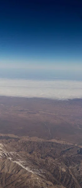 Nuages montagnes et ciel vus à travers la fenêtre d'un avion — Photo