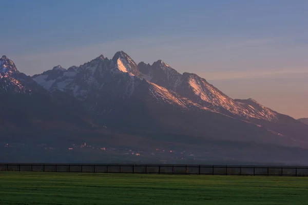 Montanhas nevadas e campo com grama verde no amanhecer — Fotografia de Stock