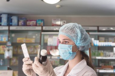 Koruyucu tıbbi maske takan, termometre ve ilaçlı genç bir kadın eczacı. Virüs kavramına karşı sağlık koruması. Seçici odaklı resim