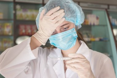 Koruyucu tıbbi maskeli ve termometresi olan genç bir kadın eczacı. Virüs kavramına karşı sağlık koruması. Seçici odaklı resim