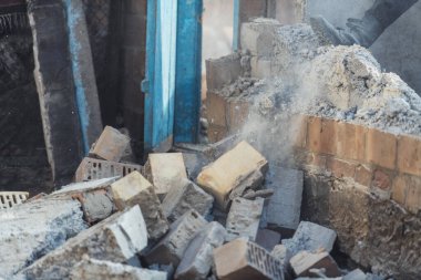 Bir adam eski bir evin duvarını yıkıyor. Toz ve tuğlalar iş başında