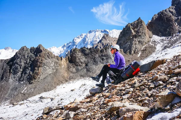 Молодая альпинистка в шлеме сидит на рюкзаке и пишет пройденный маршрут . — стоковое фото