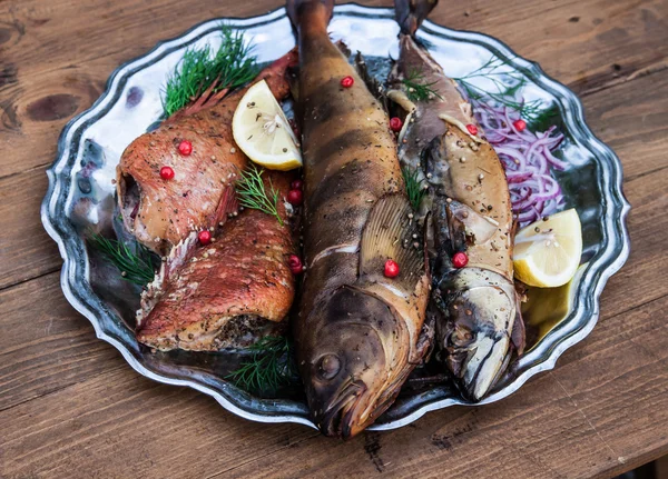 Pesce affumicato con limone e bacche su piatto di metallo, fondo di legno — Foto Stock