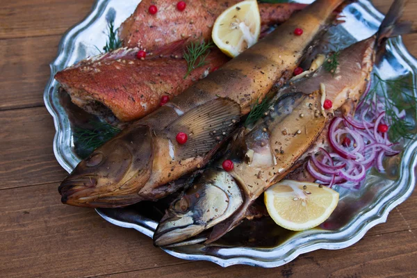 Sgombri di pesce affumicato, spigole e merluzzo bianco su placca metallica, fondo in legno — Foto Stock
