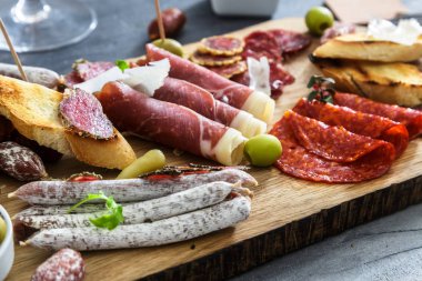 Geleneksel İspanyolca tapas - chorizo, salsichon, jamon serrano, lomo - erved zeytin ve ekmek ile ahşap tahta üzerinde tedavi et tabağı