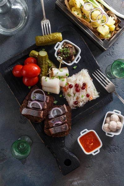 Traditional snacks salted herring with vegetables, onion, lard, bread, potato and two shots of vodka. — Stock Image Traditional snacks salted herring with vegetables, onion, lard, bread, potato and two shots of vodka. Royalty Free Stock Images