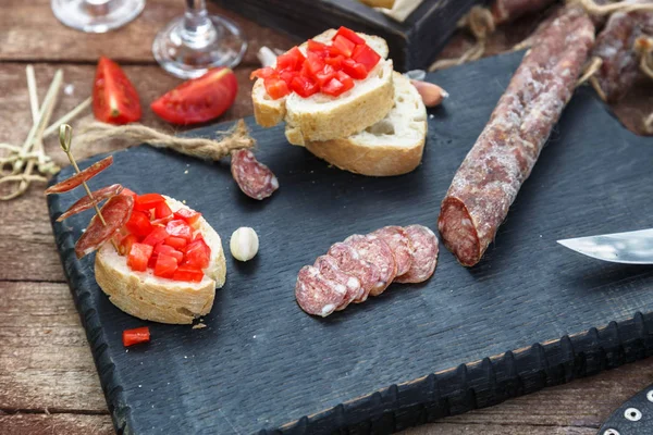 Fette di salame, baguette e pomodoro sulla tavola di legno — Foto Stock