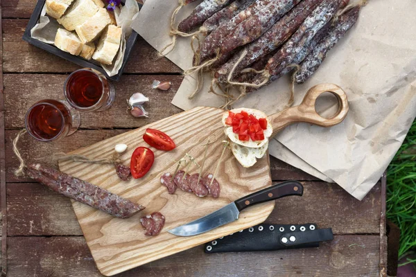 Brot, Wurst, Rotwein, Glas, Schneidebrett und Messer auf einem Holztisch für einen Imbiss in der Natur arrangiert. — Stockfoto