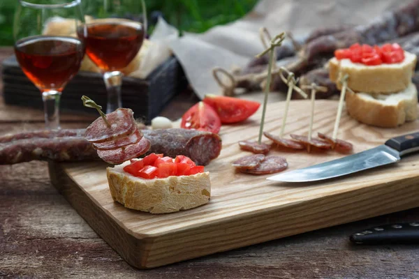 Pane, salsiccia, vino rosso, bicchiere, tagliere e coltello disposti su un tavolo di legno per uno spuntino in campagna . — Foto Stock