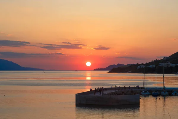 Slunce nastavení dolů nad mořem, červený disk slunce se dotýká obzoru — Stock fotografie