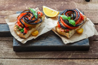 Fırında patlıcan ve biber rustik tarzı siyah ahşap gemide iki bruschettas.