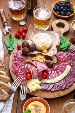 Farklı aperatifler ve mezeler: sosis, ekmek, zeytin, peynir, kestane, bezelye ve bira ahşap tahta üzerinde. Üstten Görünüm.