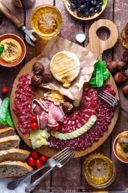 Farklı aperatifler ve mezeler: sosis, ekmek, zeytin, peynir, kestane, bezelye ve bira ahşap tahta üzerinde. Üstten Görünüm.