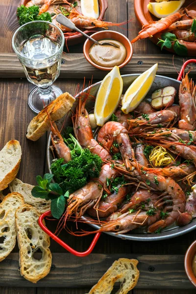 Seafood dinner. Grilled tiger prawns in grilling pan with fresh lemon, garlic, bread over wooden background, top view.