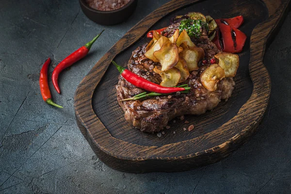 Bife suculento servido em tábua de madeira com batatas fritas crocantes e pimenta — Fotografia de Stock