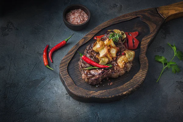 Sappige biefstuk geserveerd op houten plank met krokante aardappelchips en chili, van dichtbij bekeken — Stockfoto