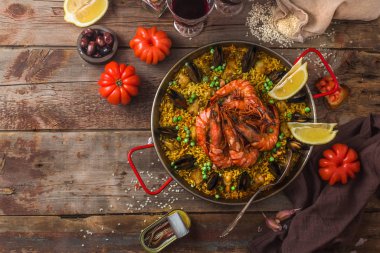 Top view of paella with seafood and lemon, wooden background