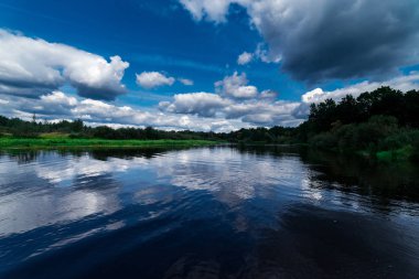 Büyük nehir ve yeşil kıyıları. Bulutlar ve mavi gökyüzü yukarıda. Hala w