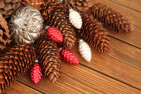 Новорічна композиція червоно-срібні іграшки з висушеними коричневими сосновими шишками на дерев'яному фоні — стокове фото