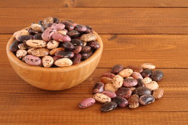 Çiğ mor, pembe, kahverengi ahşap masa, ahşap kase üzerinde kahverengi benekli barbunya fasulyesi ile bej. Portre