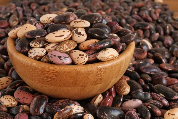 Morado crudo, rosa, beige con frijoles rojos moteados marrones en un tazón de madera en una mesa de madera marrón. Primer plano. — Foto de Stock