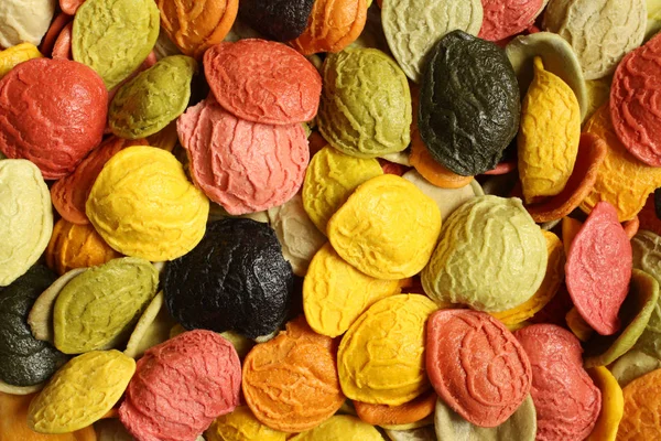 Food background - uncooked colorful durum wheat semolina orecchiette pasta with the addition of the special ingredients: dried carrot, red beet, spinaches, basil, tomatoes, turmeric powder and squid ink. — Stockfoto