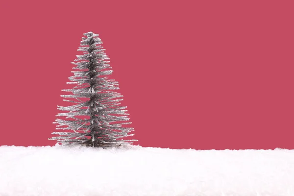 Іграшка срібна ялинка на штучному білому снігу на рожевому фоні — стокове фото