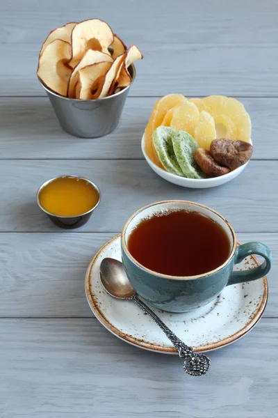 Vegetarisches Dessert: kandierte Ananasstücke, Kiwi und Mango, getrocknete Feigen, Honig, Apfelchips in kleinen Schälchen und eine Tasse schwarzen Tee auf einem grauen Holztisch. Nahaufnahme — Stockfoto