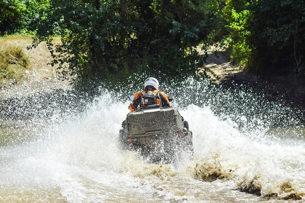 El hombre en el ATV cruza un arroyo. Caminatas turísticas en un terreno de campo a través — Foto de Stock