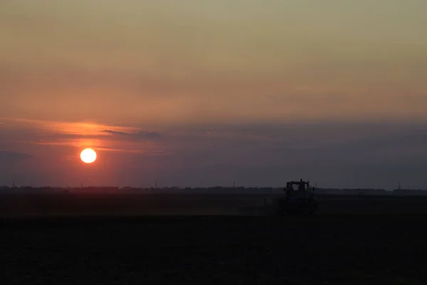 Tractor plowing plow the field on a background sunset. tractor silhouette on sunset background.