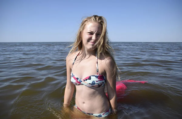 Ξανθό κορίτσι σε ένα μπικίνι στέκεται στο θαλασσινό νερό. Όμορφη νεαρή γυναίκα σε ένα πολύχρωμο μπικίνι με φόντο στη θάλασσα. — Φωτογραφία Αρχείου