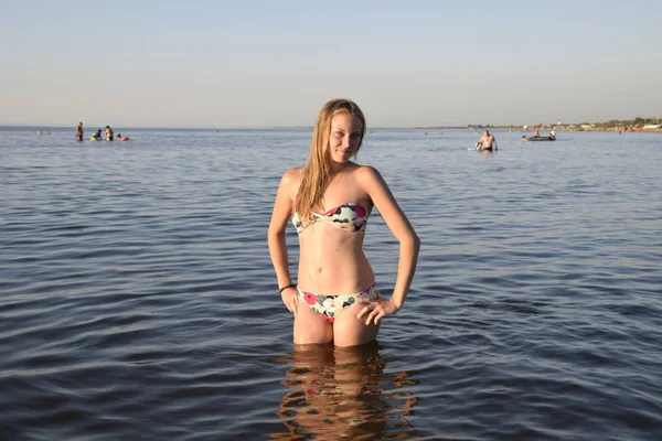 Chica rubia en bikini de pie en el agua de mar. Hermosa mujer joven en un bikini colorido sobre fondo de mar —  Fotos de Stock