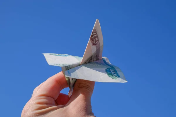 Denominations of Russian money, folded in the airplane against the blue sky in hand