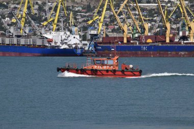 Küçük gemi hizmetinin bağlantı noktası. Kırmızı küçük tekne. Kargo bağlantı noktası bağlantı noktası ile vinç. Deniz defne ve dağlık sahil.