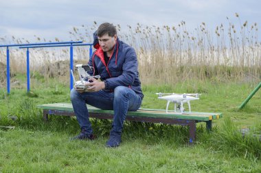 Uzaktan kumanda quadroopter onun elinde olan bir adam bir bankta oturuyor. Beyaz quadroopter hazırlamak için uçuş.