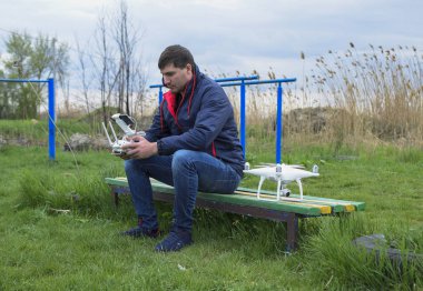 Uzaktan kumanda quadroopter onun elinde olan bir adam bir bankta oturuyor. Beyaz quadroopter hazırlamak için uçuş.