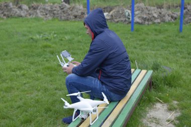 Uzaktan kumanda quadroopter onun elinde olan bir adam bir bankta oturuyor. Beyaz quadroopter hazırlamak için uçuş.