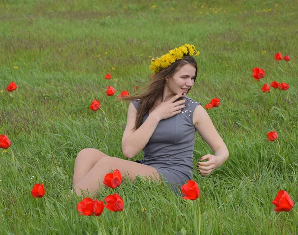 Una chica con una corona de dientes de león en la cabeza. Hermosa joven de hadas en un campo entre las flores de los tulipanes . — Foto de Stock